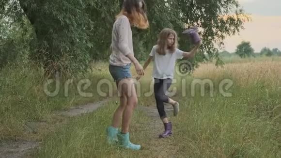 两个快乐的女孩姐妹在雨后穿着脏衣服散步孩子们说着笑有趣地从靴子里倒水视频的预览图