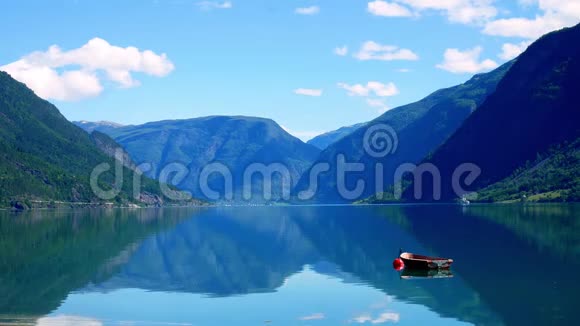 在挪威的Lustrfjord平静的水域中一艘小木船停泊在一个红色的浮标上倒影着群山和蓝天视频的预览图