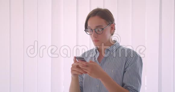年轻英俊的白种人商人戴着眼镜用手机站在办公室的室内特写视频的预览图