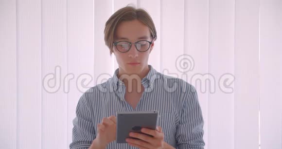 年轻英俊的白种人商人用平板电脑站在办公室的室内特写照片视频的预览图