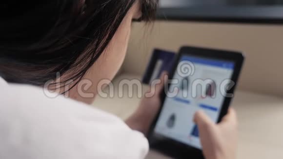 女孩用数字平板电脑制作网上购物概念黑发女人躺在生活方式沙发上看网上商店视频的预览图