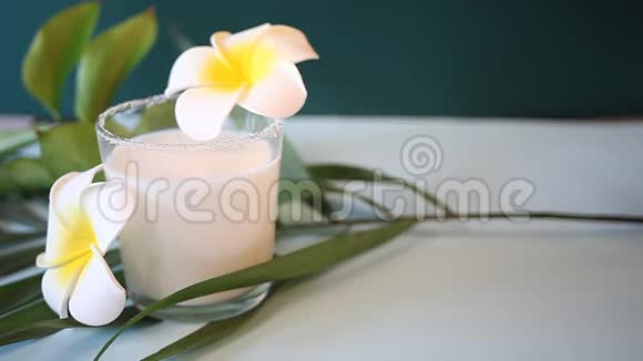 女人手把一杯椰奶放在桌子上上面放着花梅花和棕榈叶视频的预览图