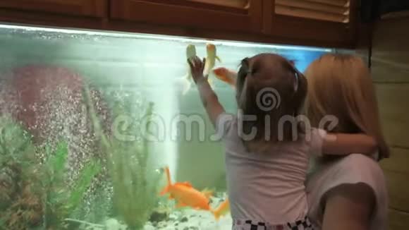 一个抱着一个小女孩的女人站在一个大型水族馆里好奇地考虑游泳鱼视频的预览图