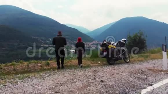 几个骑着冒险摩托车的摩托车旅行者站在远处山城背景后景视频的预览图
