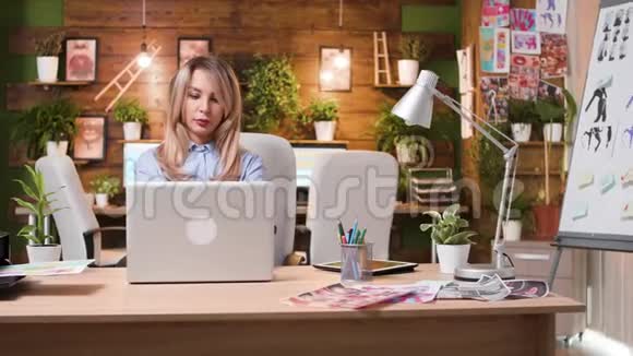 一位美丽的金发女人在她的电脑上工作在专业的创意工作场所视频的预览图