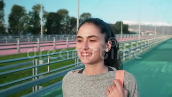 快乐的年轻女运动员走在露天体育场的跑道上微笑着视频的预览图
