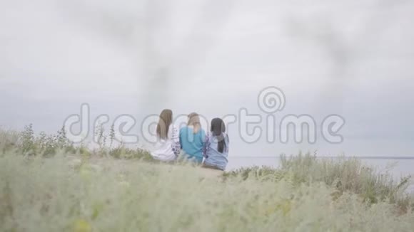 三个穿着夏日长礼服的年轻女朋友在湖边或视频的预览图
