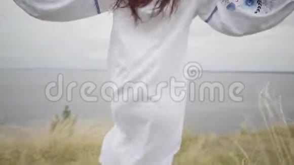 一个黑发女孩穿着白色的夏装在高高的草丛中刺绣手里拿着一束草河上视频的预览图