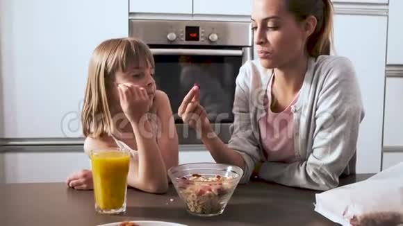 美丽的母亲和女儿在家里的厨房里吃着碗里的麦片视频的预览图
