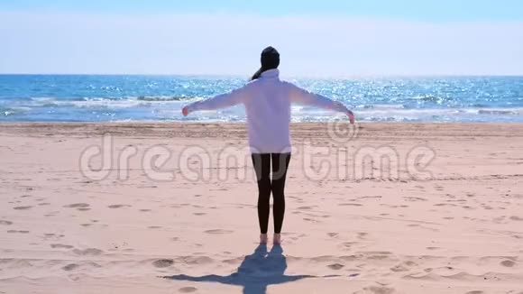 穿着帽衫和帽子的女人正在海沙滩做瑜伽后景视频的预览图