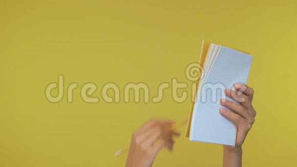 女性手在一个孤立的黄色背景上用铅笔在笔记本上做笔记4K视频的预览图