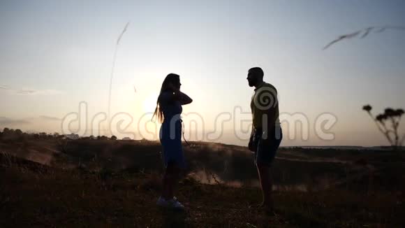 一对相爱的年轻夫妇的剪影在黄昏的夕阳灯光下与天空牵手农村的夫妇视频的预览图