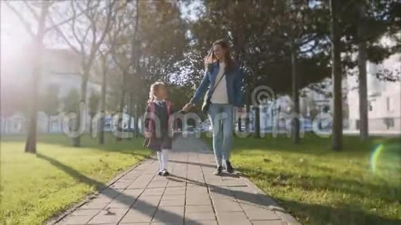 年轻的妇女和女儿穿着校服在阳光明媚的天气里散步稳重视频的预览图