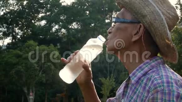 资深亚洲农民在花园里喝一些瓶子里的水视频的预览图