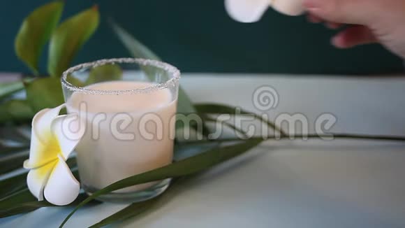 女人手把花梅花放在椰奶杯上背景上的棕榈叶视频的预览图