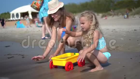 母亲和女儿在海岸线上玩海沙和玩具车视频的预览图
