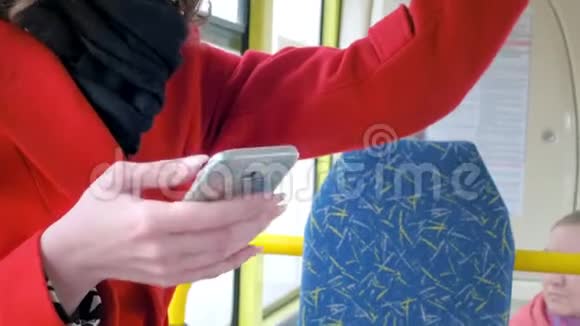 一个穿红色外套的优雅年轻女孩的肖像在公共交通中使用智能手机打印总线上的短信视频的预览图