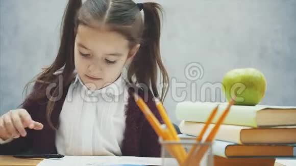 灰色背景的女学生在这段时间里他坐在桌子旁拿起一本笔记本视频的预览图