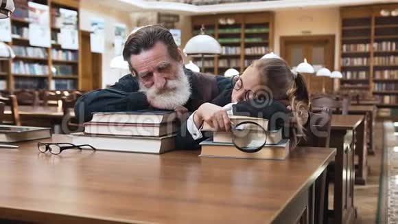 疲惫的胡子老人和他十几岁的漂亮孙女睡在图书馆的书上视频的预览图