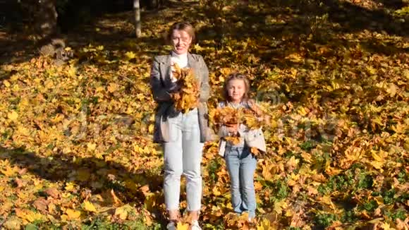 妈妈和她的女儿可爱的小女孩在秋天的公园里扔落叶的黄枫叶家庭幸福视频的预览图