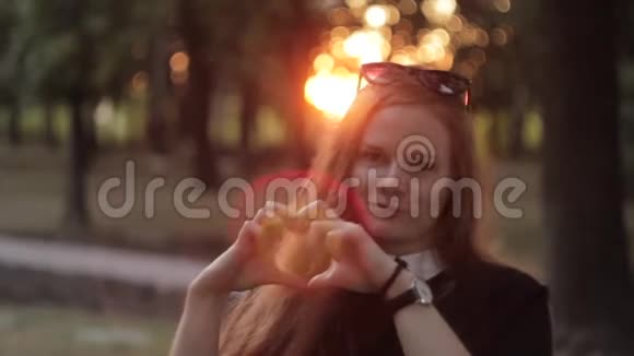 美丽的女人在夕阳下用双手做心形视频的预览图