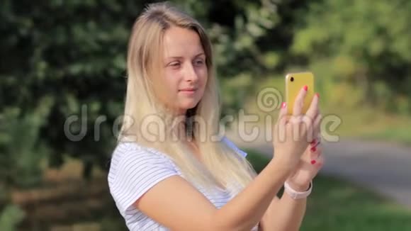 一个手里拿着智能手机的年轻女人站在一个夏天的公园里视频的预览图
