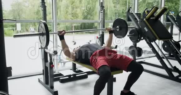年轻运动员在健身房做板凳压人躺在长凳上用杠铃做运动慢动作视频的预览图