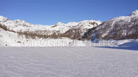 在阳光明媚的冬日在山谷上覆盖着雪的冰湖上空飞行欧洲阿尔卑斯山脉户外爱好者视频的预览图