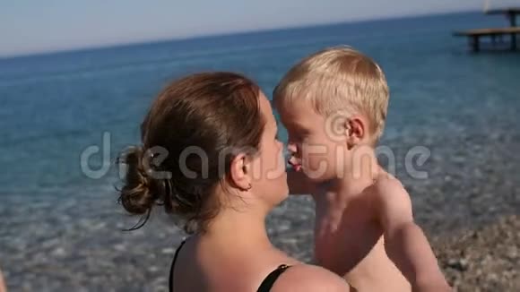 母亲在海边的海滩上拥抱和亲吻儿子视频的预览图
