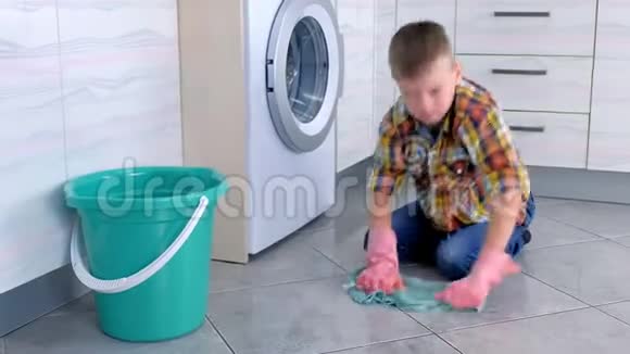 穿着橡胶手套的疲惫男孩在厨房里洗地板看着相机儿童的家庭责任视频的预览图