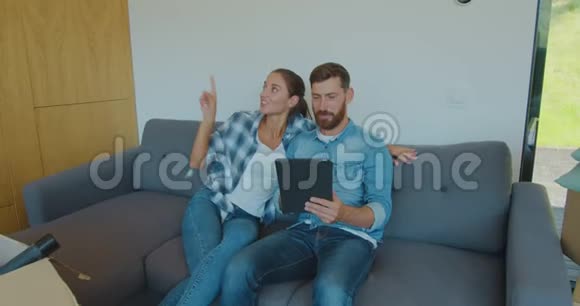 幸福的一对房客坐在沙发上在新房子搬家的日子里使用数字平板电脑男人和女人都放松了视频的预览图
