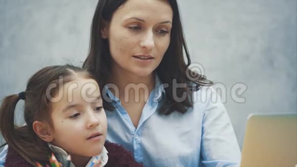 关上一个女学生和他的母亲坐在桌子旁看着笔记本电脑玩得开心花时间视频的预览图
