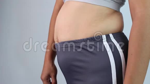 女性手捏过多腹部脂肪的特写镜头隔离在灰色背景上女人胖肚子肥胖与超重视频的预览图