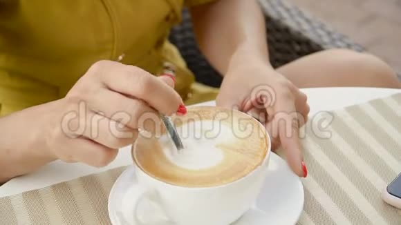 女孩正用勺子在白色的杯子里搅拌卡布奇诺视频的预览图