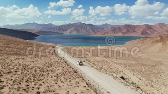 在4x4路的高空汽车沿着砾石小径驶向干旱山区的湖泊帕米尔公路丝绸之路视频的预览图