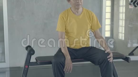 亚洲老人在健身房锻炼后累了亚洲老人汗流浃背地坐着表情疲惫锻炼后呼吸急促视频的预览图