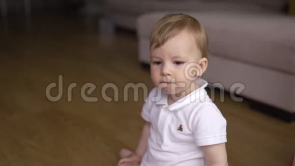 小男孩坐在家里的地板上感到困倦和好奇孩子穿白色t恤身体马球视频的预览图
