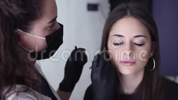 戴着黑色手套的卷发的年轻女子在美容店里扭着客户的眉毛年轻的女人视频的预览图