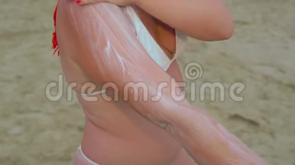 一位身穿白色泳衣的红发年轻女子正在海边给身体涂防晒霜视频的预览图