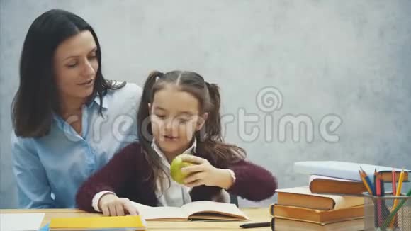 勤奋的女儿读书妈妈带了一个绿苹果坐在灰色背景上视频的预览图