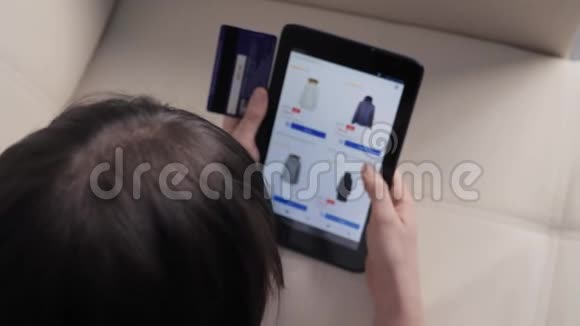 女孩用数字平板电脑制作网上销售购物概念黑发女人躺在沙发上看着网上商店付钱视频的预览图