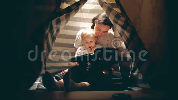 晚上妈妈和她的小宝宝在一个舒适的灯光下一起读一本书视频的预览图