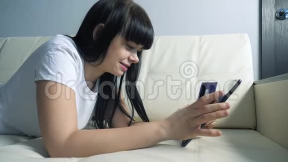 女孩用数字平板电脑制作网上销售购物概念黑发女人躺在沙发上看着网上商店通过支付视频的预览图