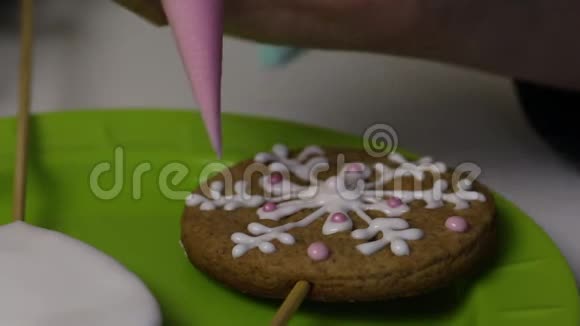 一个女人在姜饼饼干上用粉红色糖霜的形式餐盘附近有带糖霜的饼干视频的预览图