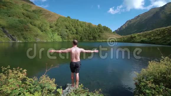 徒步旅行者伸开双臂待在湖边一个年轻的徒步旅行者走到山上的湖边伸出手臂视频的预览图