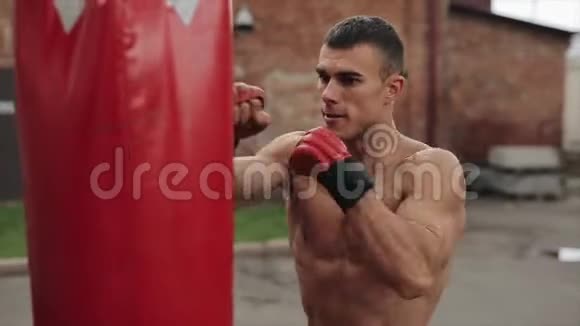 肌肉男拳击手练习拳打脚踢的近侧视图拳袋在户外棕色墙壁视频的预览图