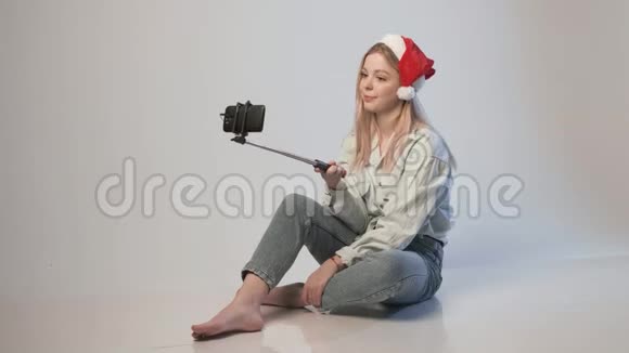 戴着圣诞帽的年轻女孩用智能手机录制自拍棒视频视频的预览图