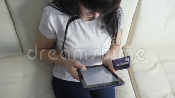 女孩用笔记本电脑数字平板电脑制作网上销售购物概念黑发女人躺在沙发上看着商店的生活方式视频的预览图