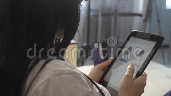 女孩制作网上销售生活方式购物概念与笔记本电脑数字平板电脑黑发女人躺在沙发上看着商店视频的预览图