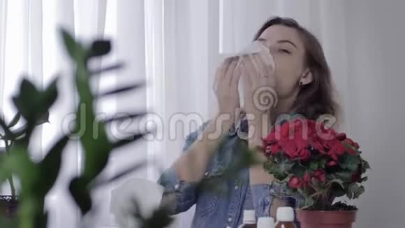 生病的年轻女性坐在桌旁服用药物由于季节性原因她们会打喷嚏并用手帕打鼻子视频的预览图